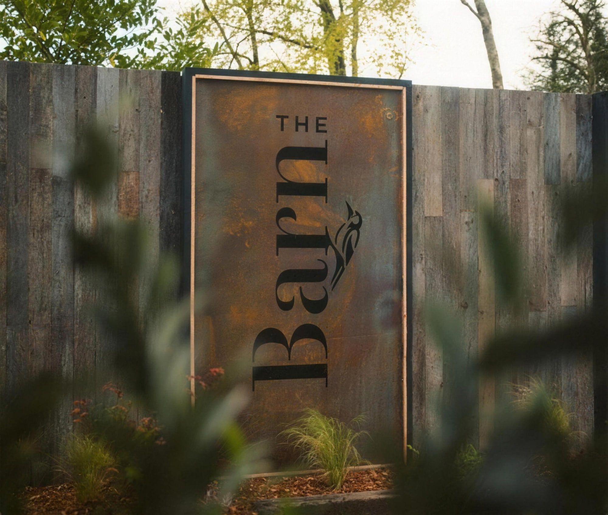 The weathered-steel "The Barn" sign on the timber boundary