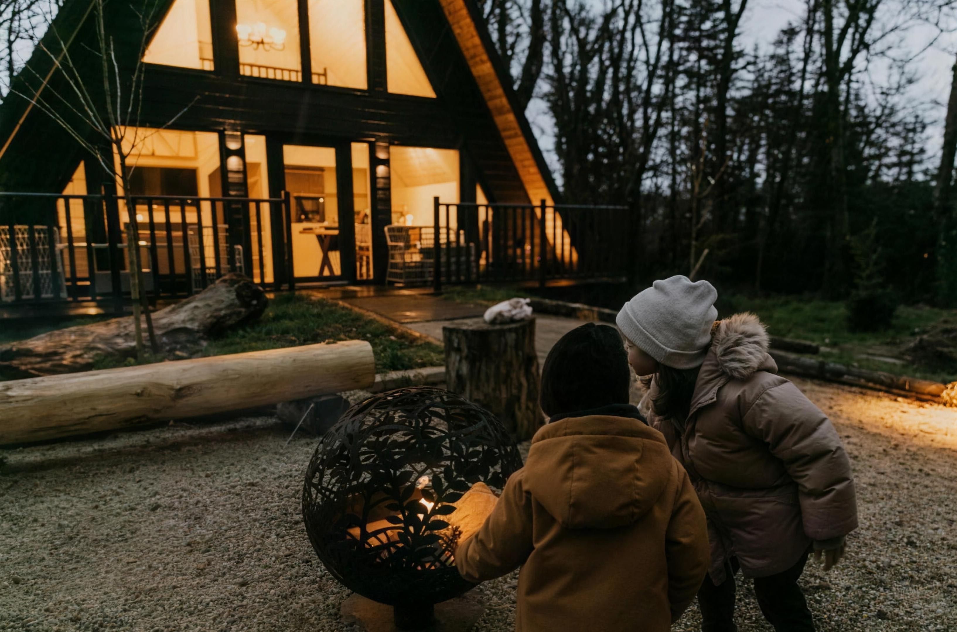 Children warming up at the fire pit outside a glowing lodge at dusk