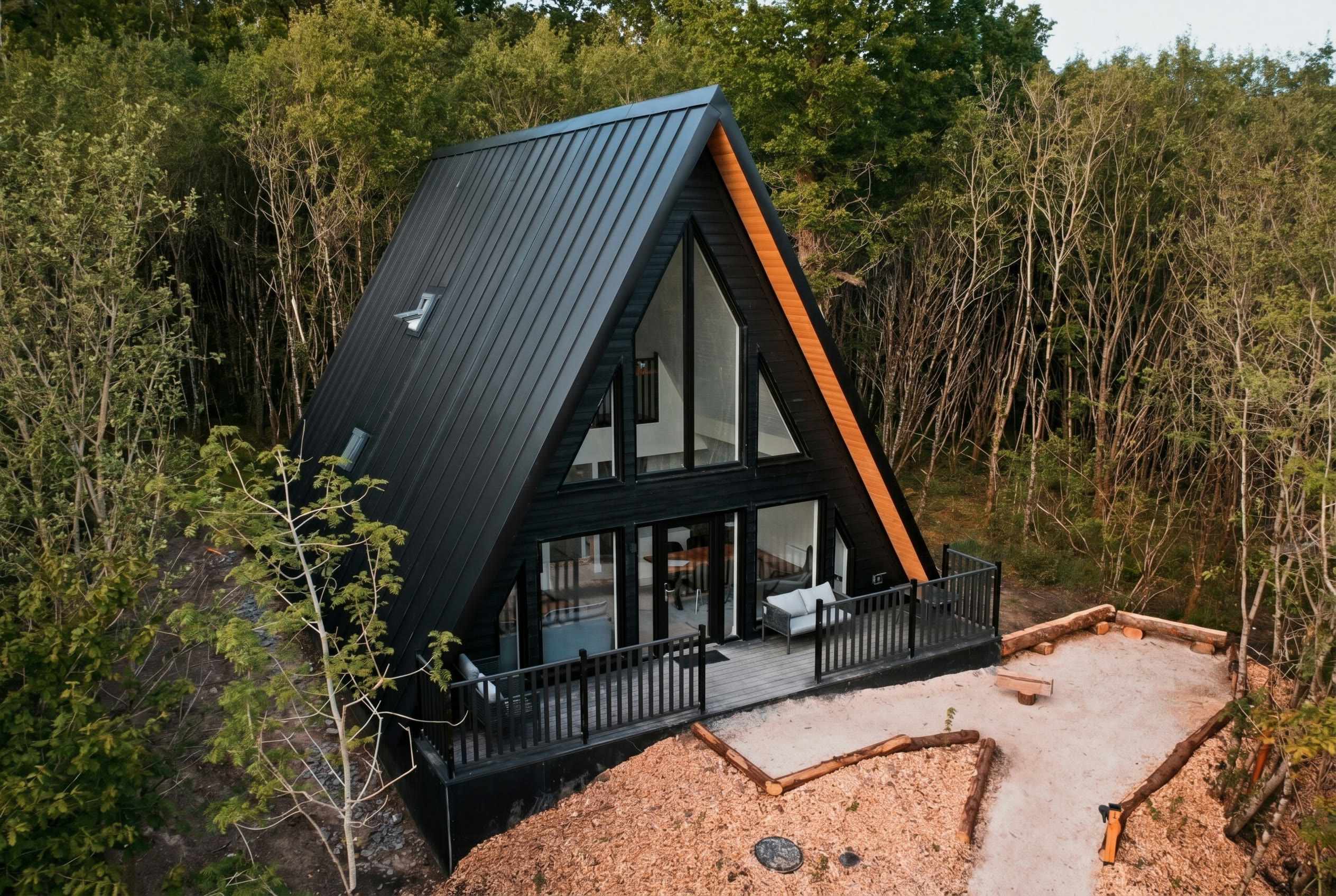 The black-timber A-frame Habitat lodge glowing at dusk in the birch wood