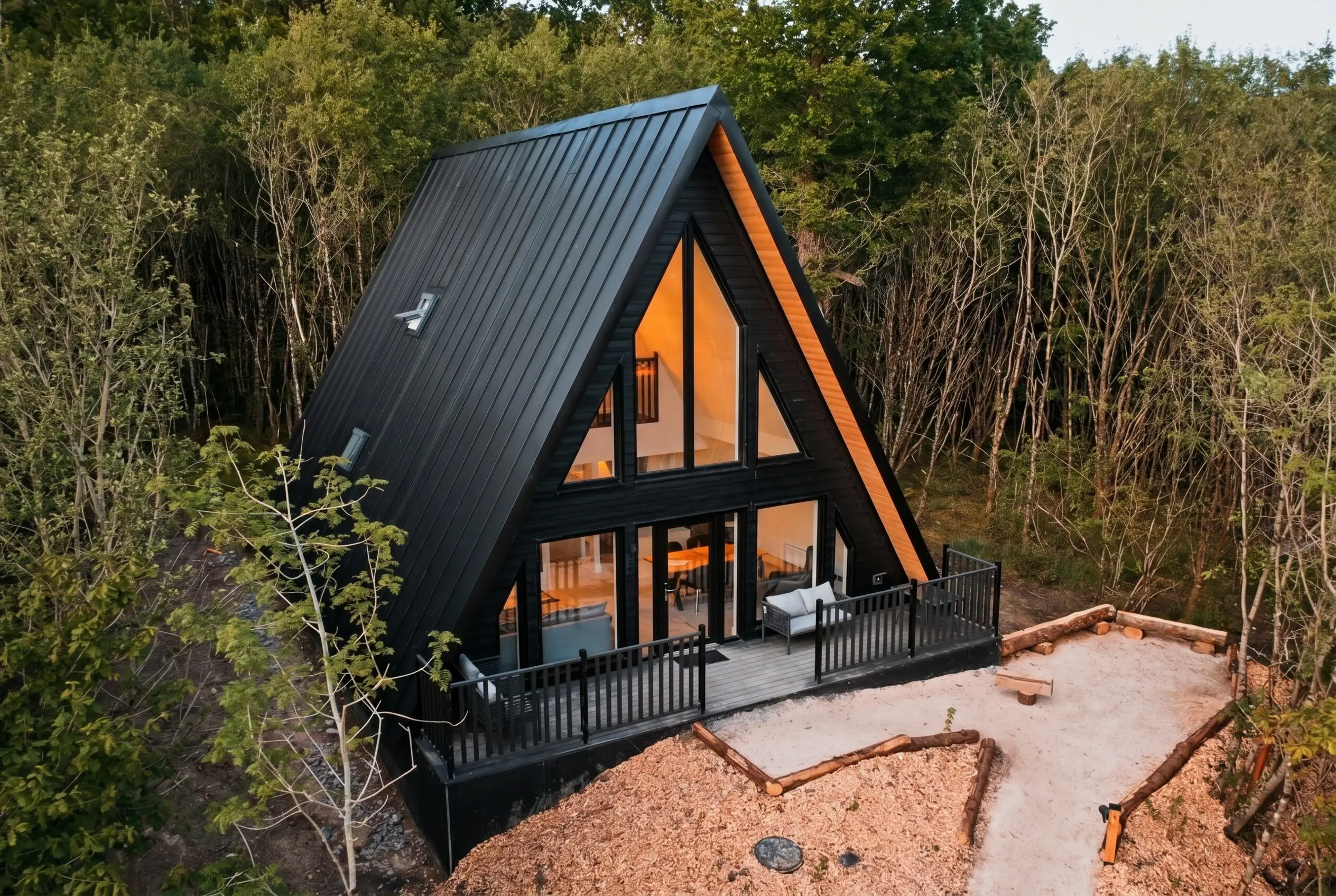 Black timber A-frame lodge glowing at dusk among the trees at Drumhierny